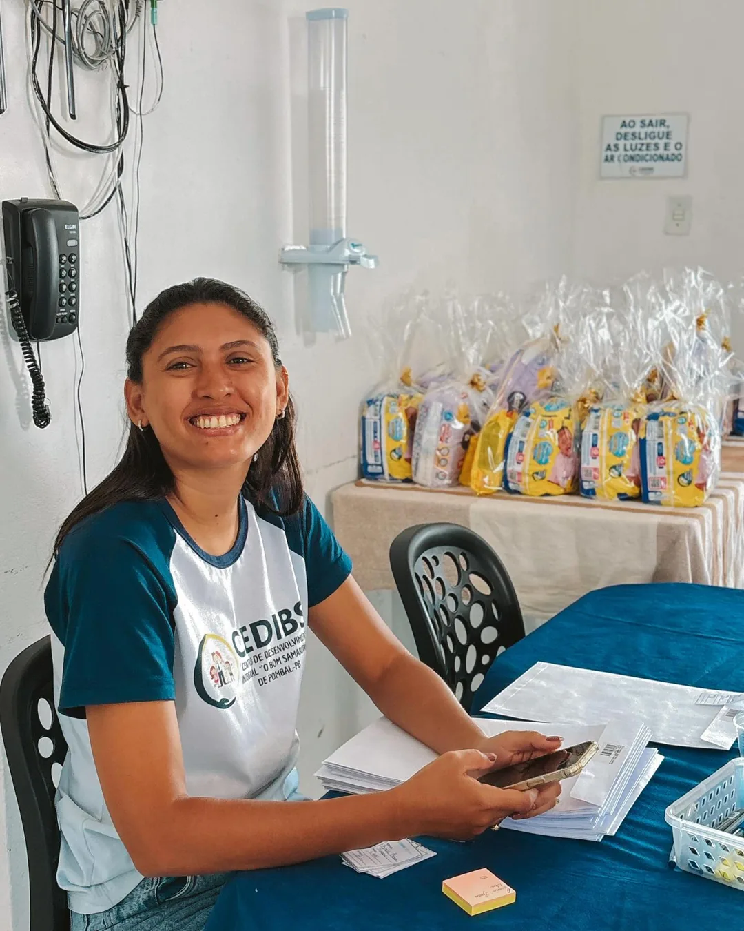 Voluntária sorri na recepção, ao lado de kits preparados para as famílias