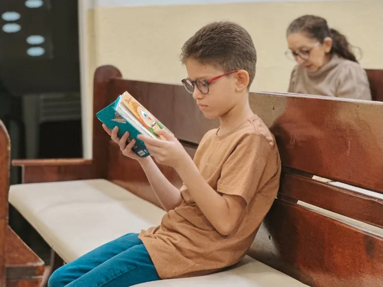 A boy sitting on a church pew, reading attentively